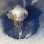 volcano erupting with an ash cloud over an island