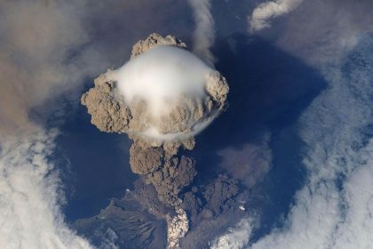 volcano erupting with an ash cloud over an island