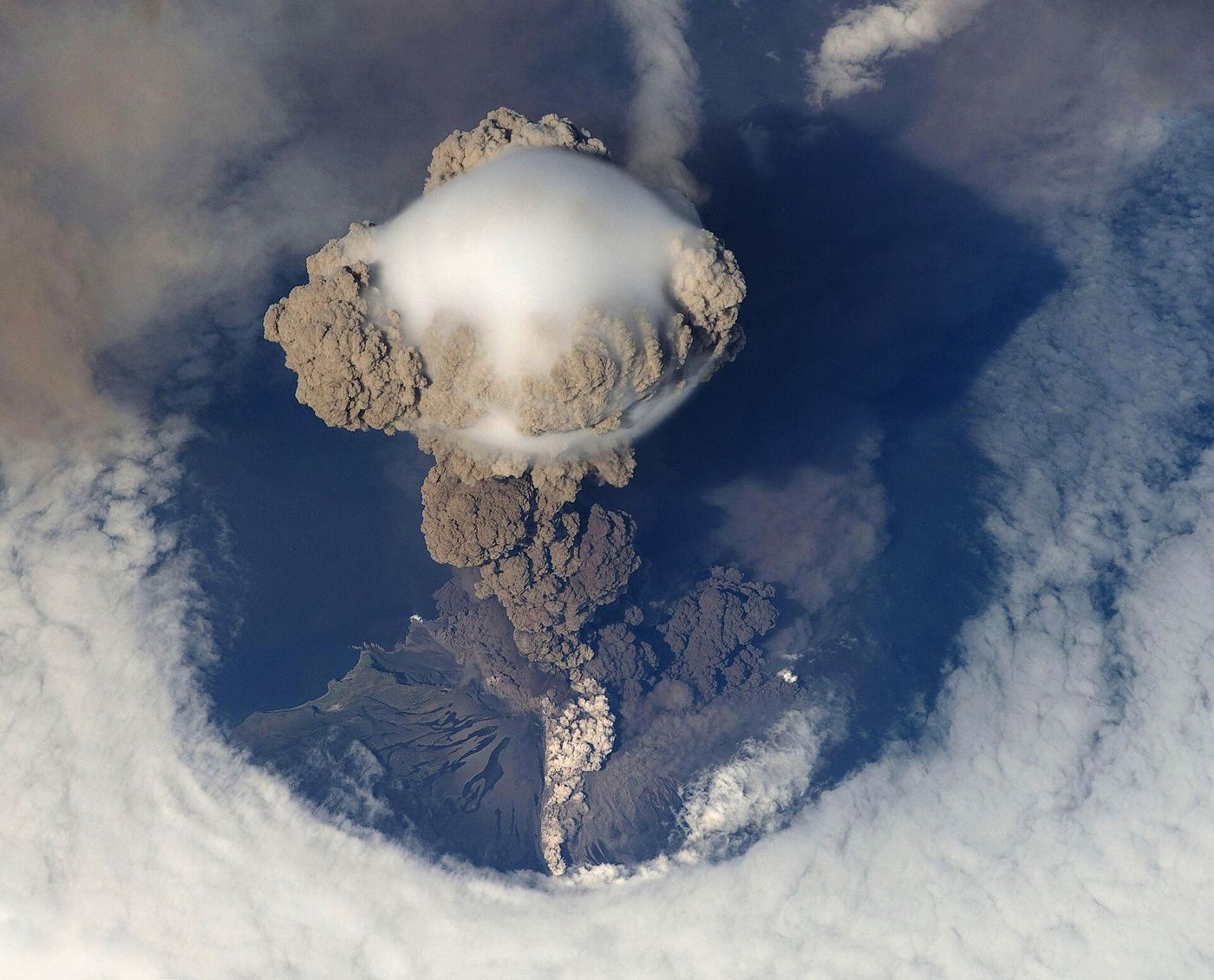 volcano erupting with an ash cloud over an island
